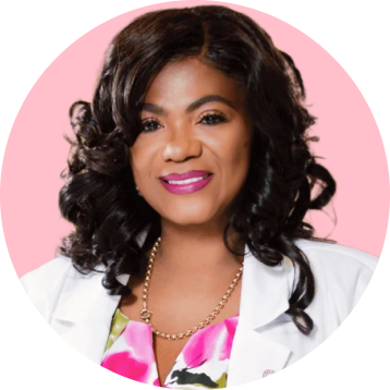 A woman with curly hair smiles, wearing a white coat and colorful top.